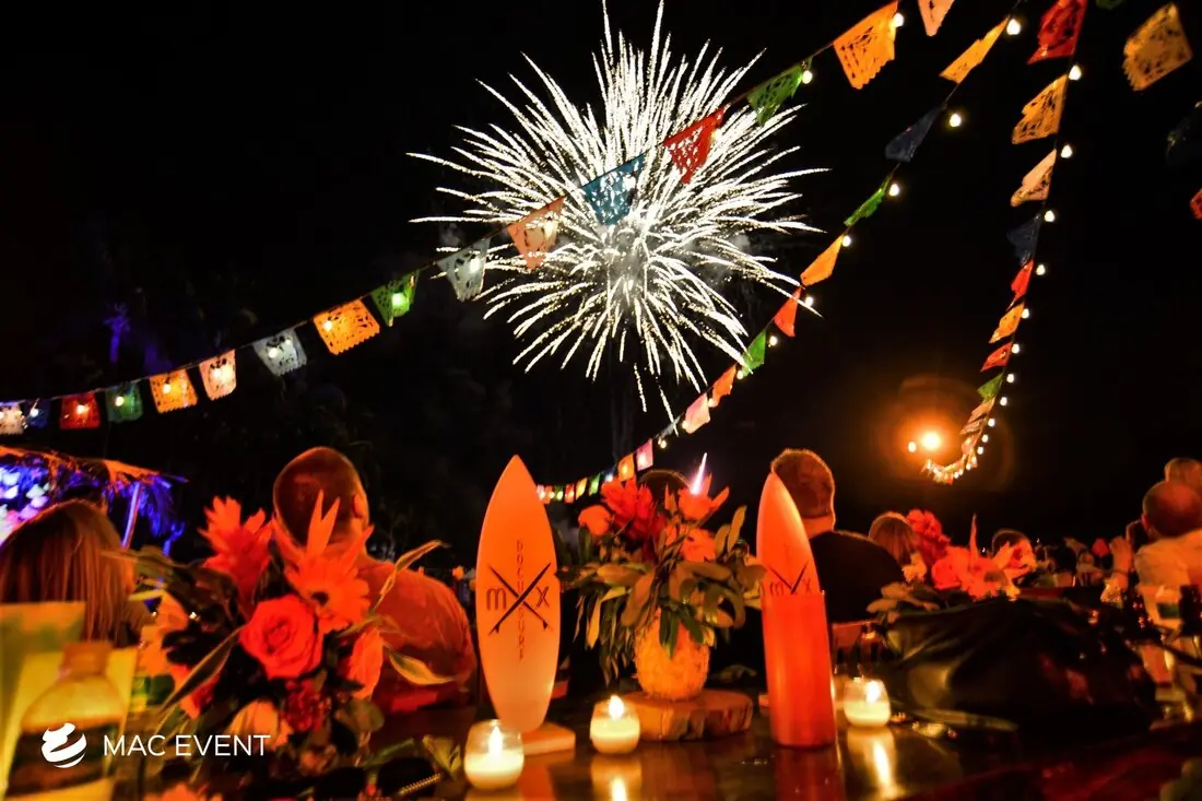 A wedding reception with colorful Mexican-style decorations, string lights, and candles, as fireworks explode in the sky, creating a vibrant and festive scene.